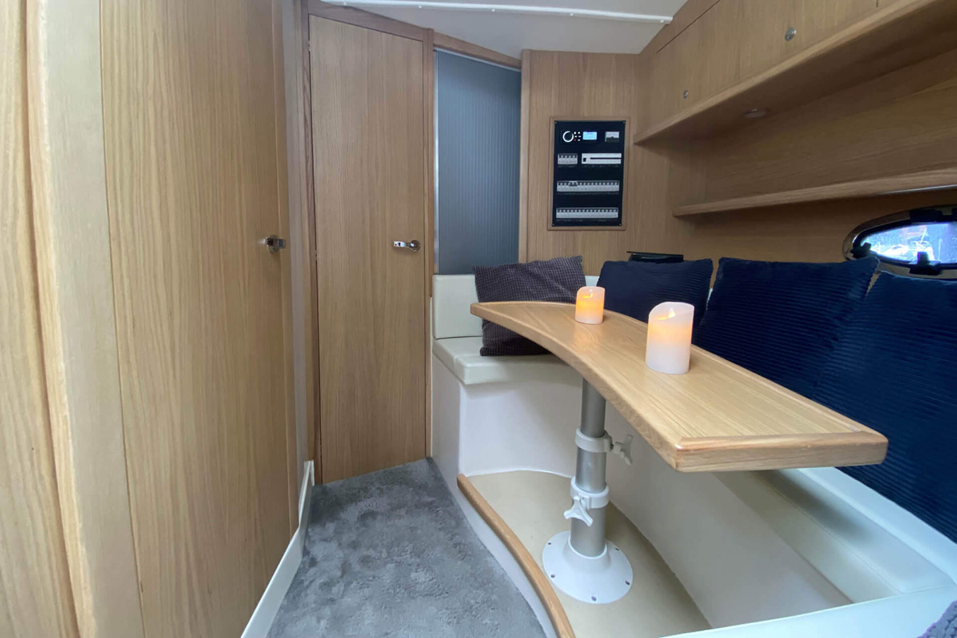 Ugodna i osvijetljena blagovaonica unutar moderne sportske jahte, s drvenim stolom s dvije svijeće, udobnim sjedalima s plavim jastucima i oblogama od svijetlog drveta