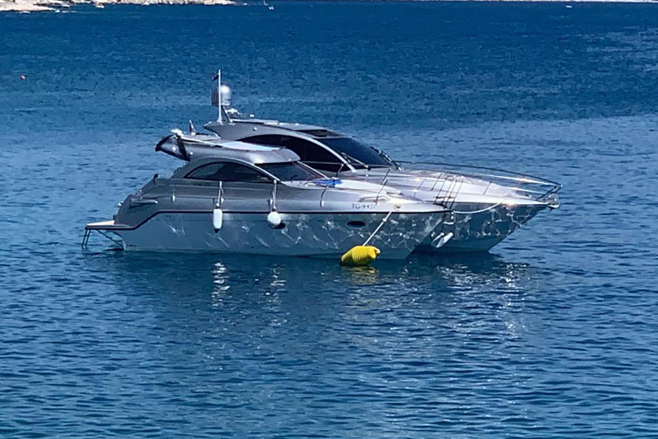 Srebrna sportska jahta usidrena u mirnom plavom moru s žutom plutačom vezanom za pramac