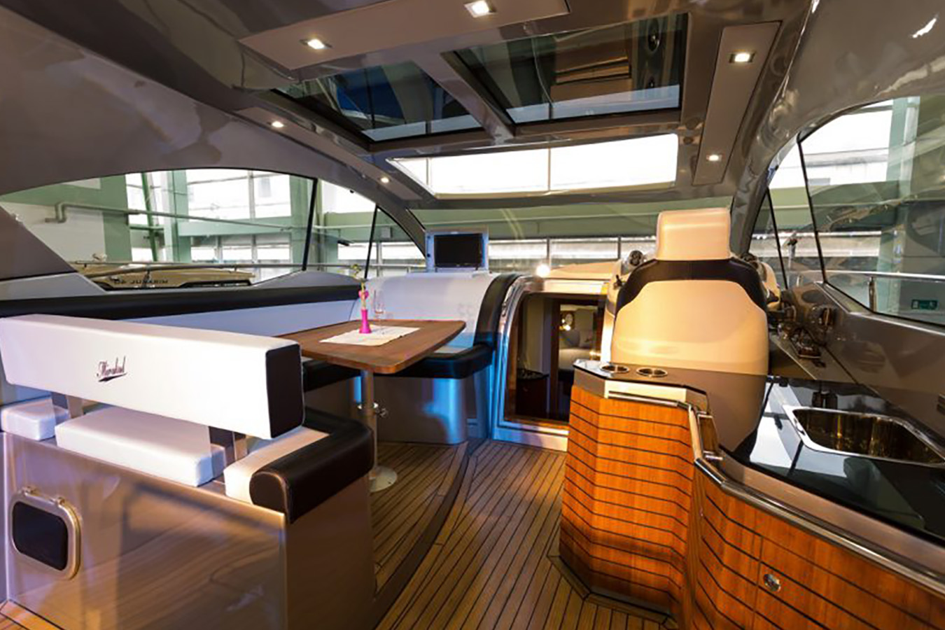 Svijetao kokpit Mirakul 40 s drvenim stolom, U-sjedištem i bočnom kuhinjskom pločom; iznad stakleni krov, naprijed ulaz u kabine — profinjena raspodjela prostora luksuzne jahte
