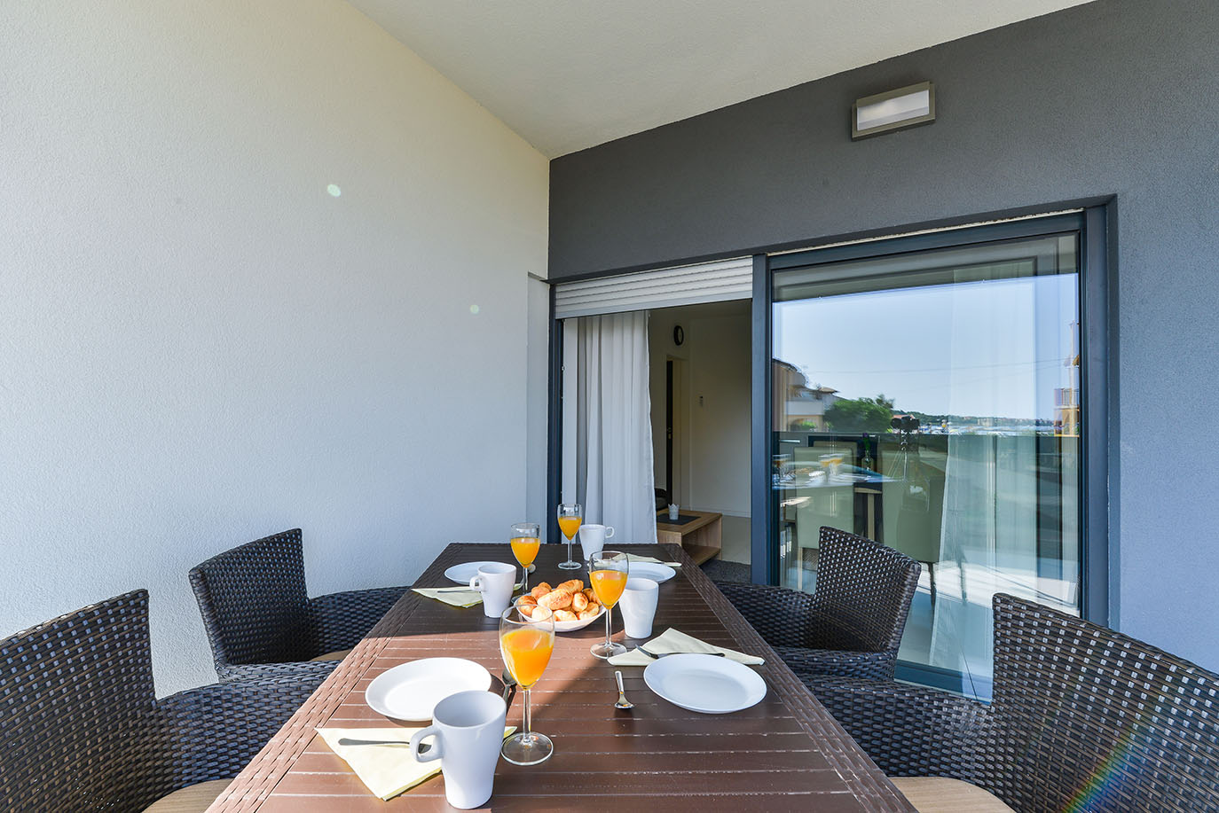 Moderan balkon s doručkom, postavljenim sokom od naranče, kroasanima i bijelim posuđem, s pogledom na more, što ukazuje na luksuzni smještaj