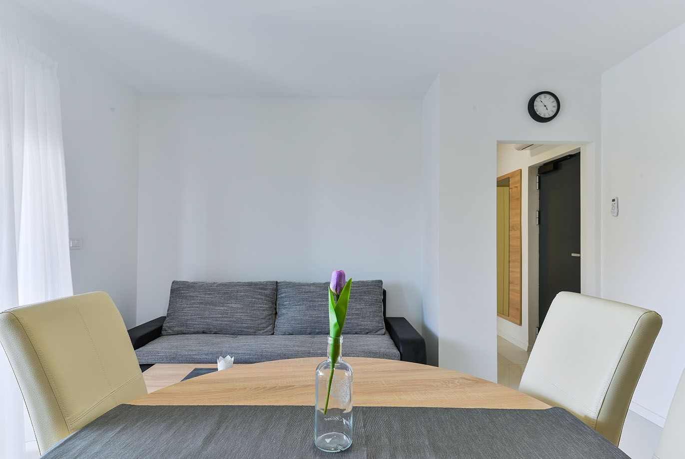 Moderan dnevni boravak i blagovaonica u apartmanima Vir s udobnom sivom garniturom, drvenim stolom i ljubičastim tulipanom