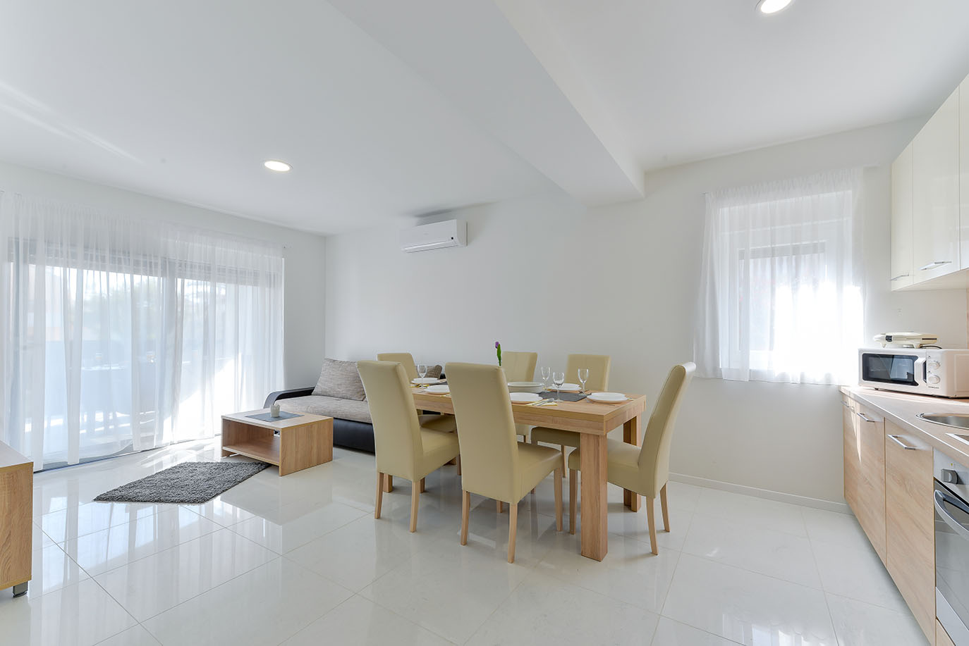 Svijetao i moderan otvoreni prostor koji obuhvaća udoban kauč, drveni stol za blagovanje sa šest stolica i mali kuhinjski kutak, savršen za luksuzni smještaj