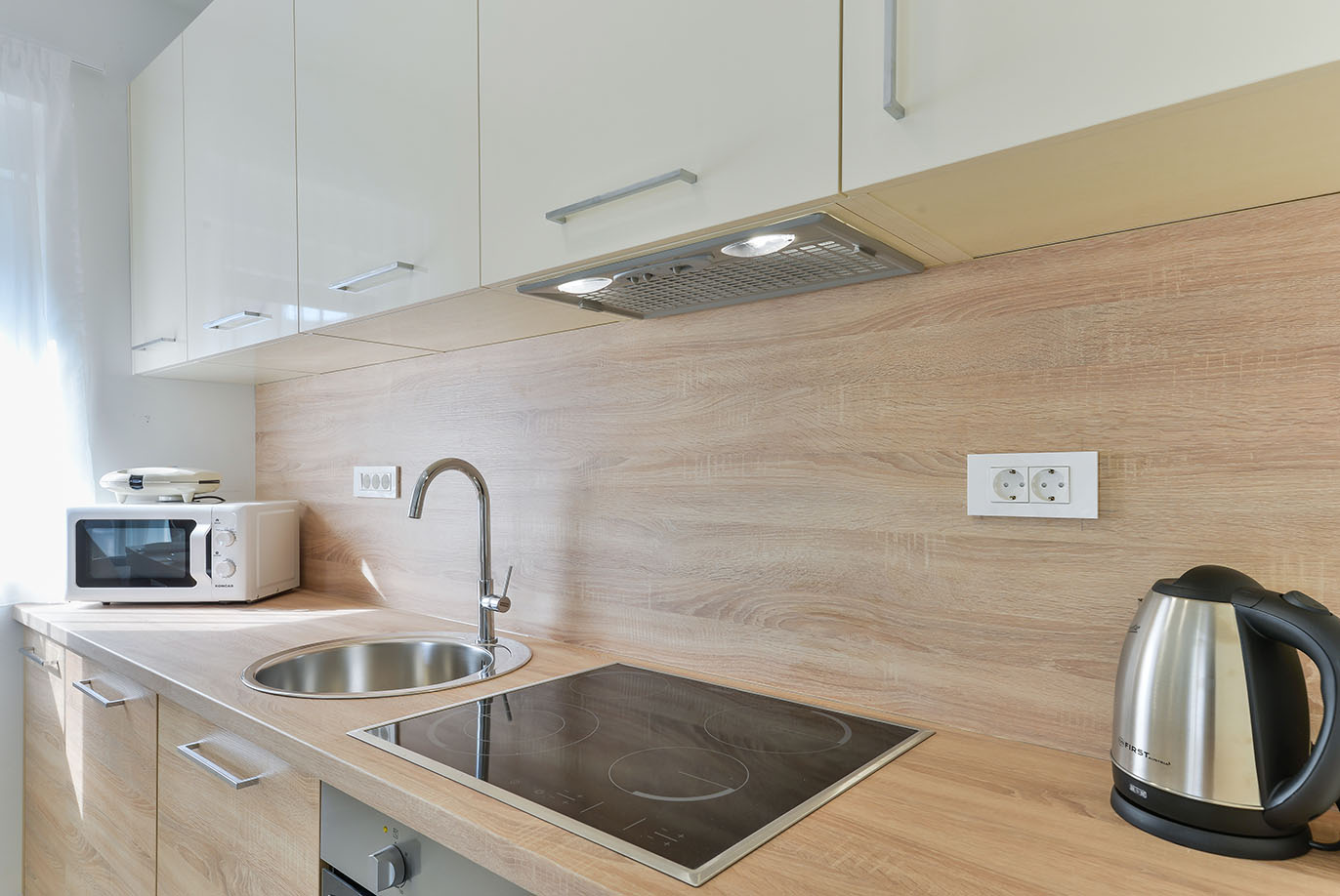 Moderna kuhinja sa svijetlim drvenim završecima, indukcijskom pločom i mikrovalnom pećnicom, idealna za samostalno kuhanje u luksuznom smještaju