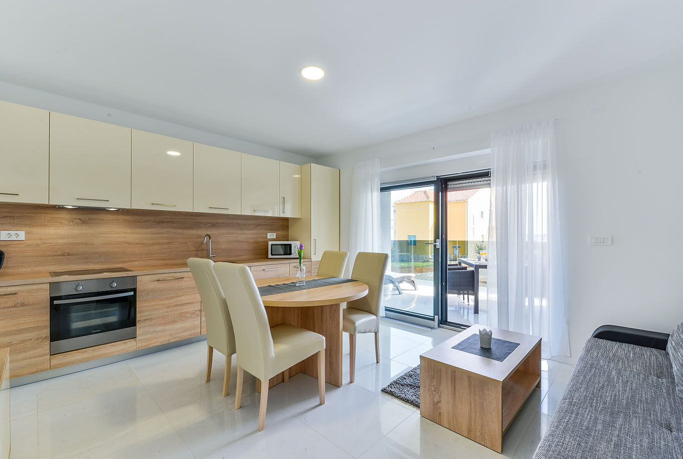 Moderna kuhinja i blagovaonica otvorenog plana u jednom od udobnih apartmana Vir, s krem ormarićima, drvenim radnim pločama i izlazom na terasu