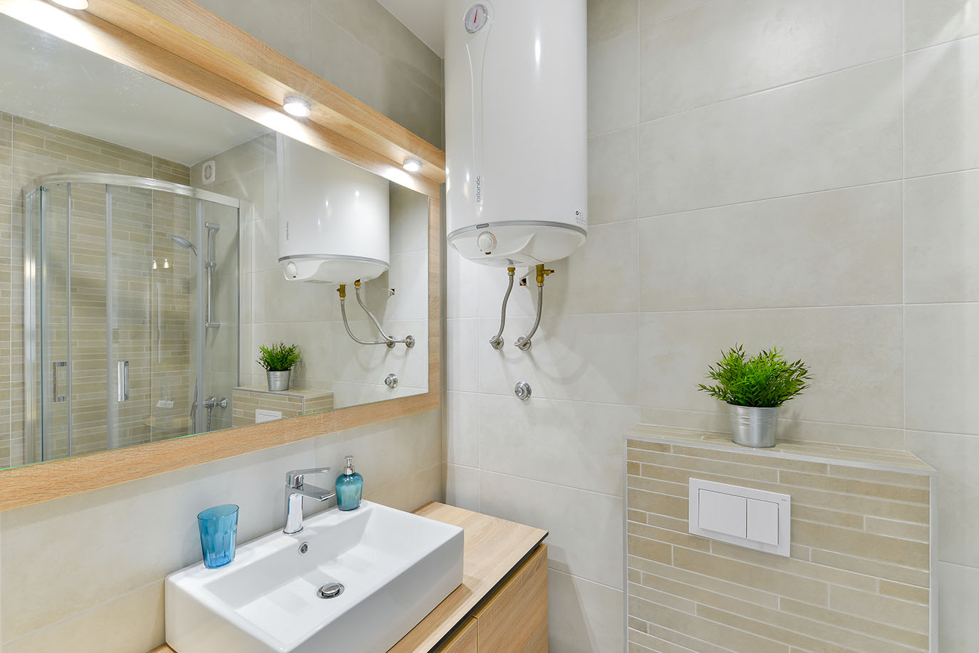 Suvremena kupaonica, savršena za luksuzni smještaj, opremljena elegantnim bijelim umivaonikom, velikim ogledalom i zidnim bojlerom