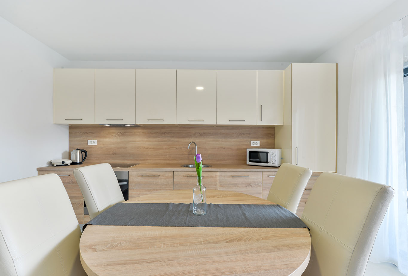 Svjetla, moderna kuhinja i blagovaonica s krem ormarićima, drvenim radnim pločama, okruglim stolom za objedovanje i krem stolicama, što je karakteristično za apartmane Vir