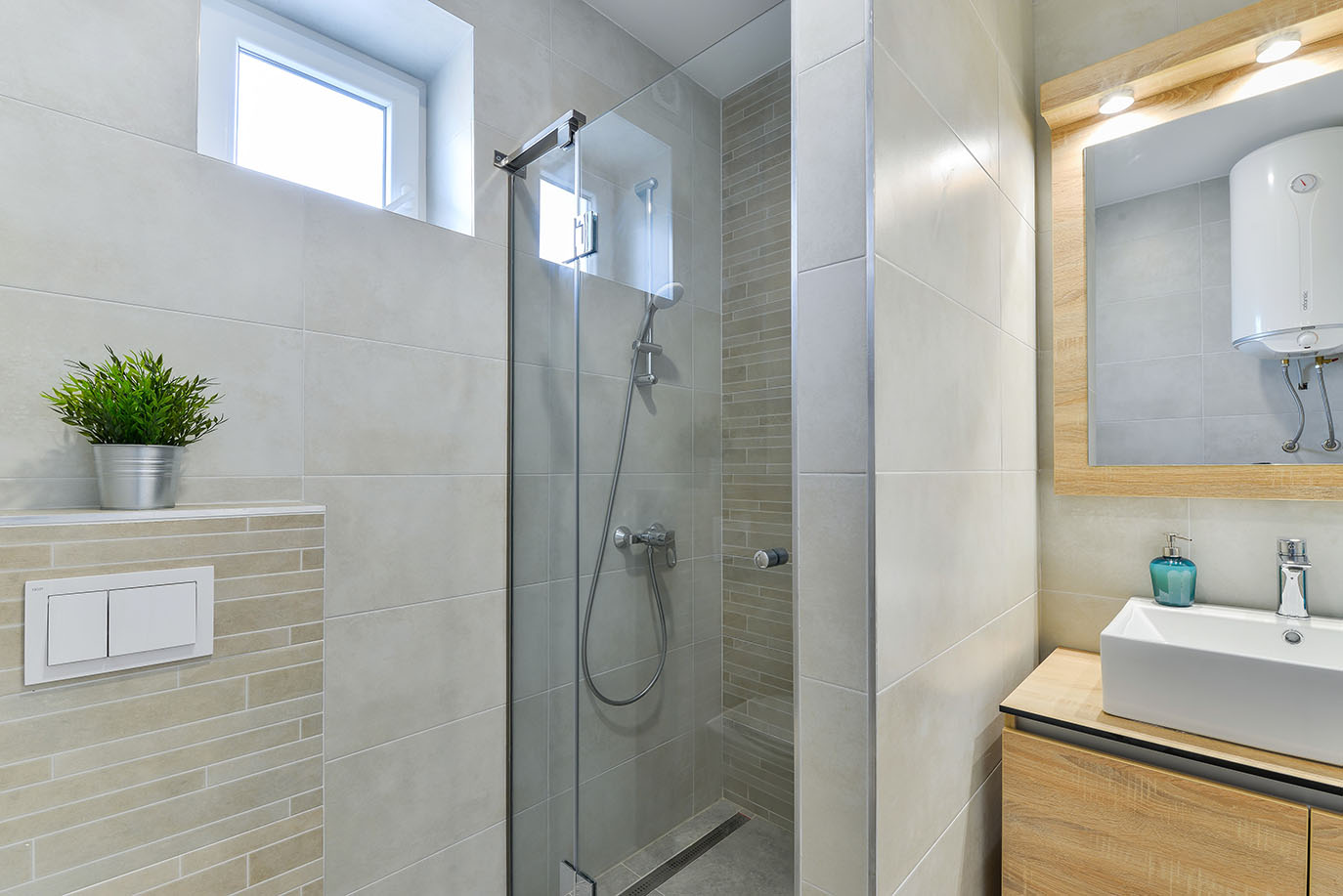 Moderna, popločana kupaonica s tuš kabinom od stakla, bijelim umivaonikom na drvenom ormariću i osvijetljenim ogledalom, tipična za luksuzni smještaj