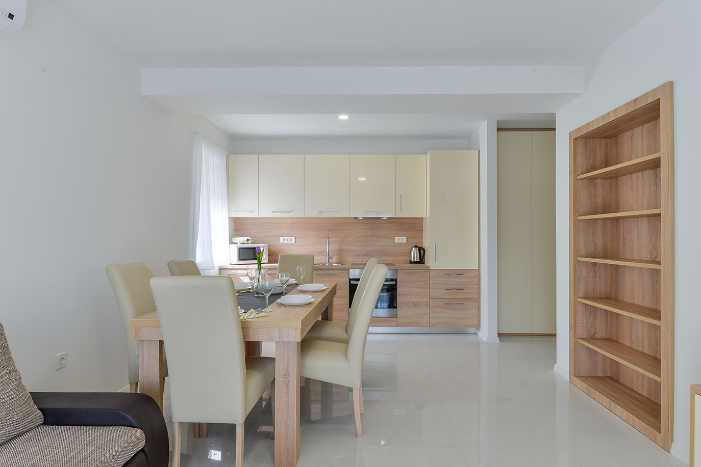 Moderna i svijetla kuhinja s blagovaonicom otvorenog plana, opremljena svijetlim drvenim stolom, bež stolicama i potpuno namještenim kuhinjskim elementima, idealna za luksuzni smještaj