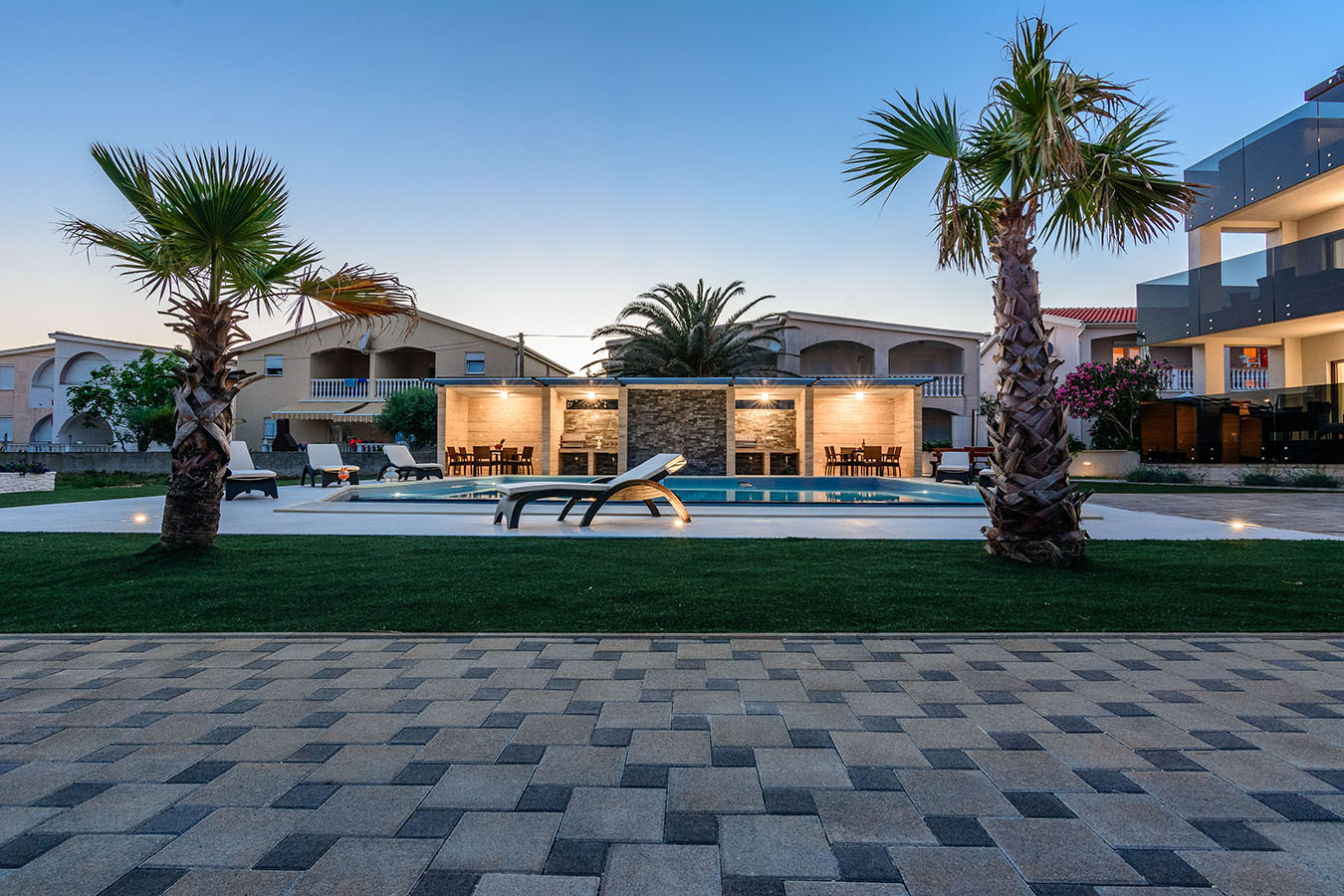 Večernji prizor kompleksa Resort Mirakuls bazenom, palmama i uređenim vanjskim blagovaonicama, karakterističan za luksuzni smještaj