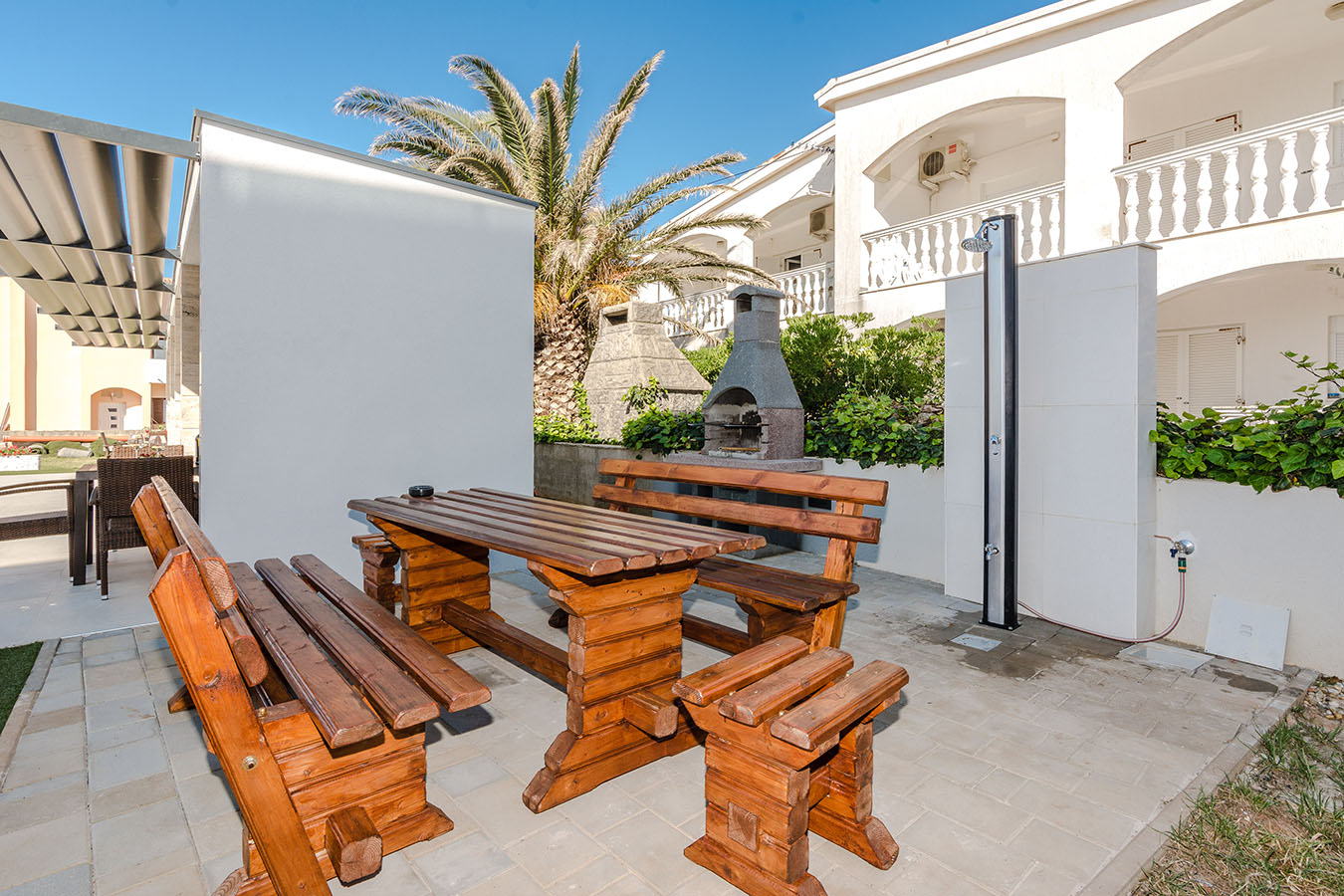 Drvene klupe i roštilj s vanjskim tušem u dvorištu – detalj sadržaja koji upotpunjuje apartmane na Viru