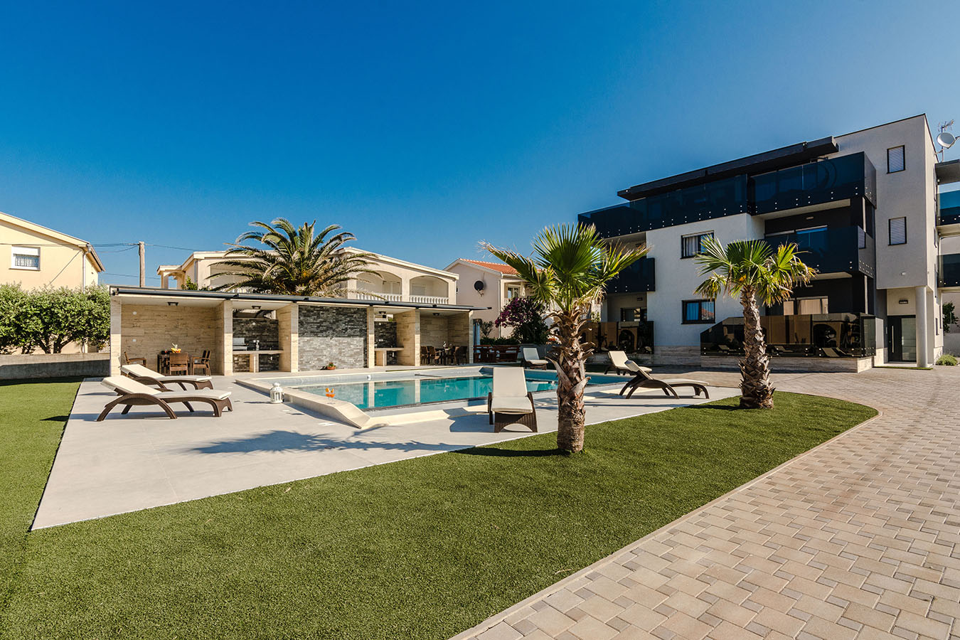 Živahno vanjsko područje u Resortu Mirakul, sa svjetlucavim bazenom, udobnim ležaljkama i bujnim palmama pod vedrim plavim nebom