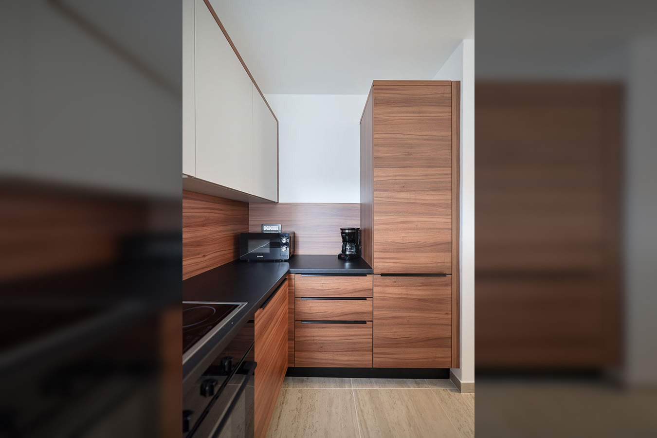 Moderna kuhinja s drvenim i bijelim ormarićima, crnom radnom pločom, mikrovalnom pećnicom i aparatom za kavu, dio luksuznog smještaja