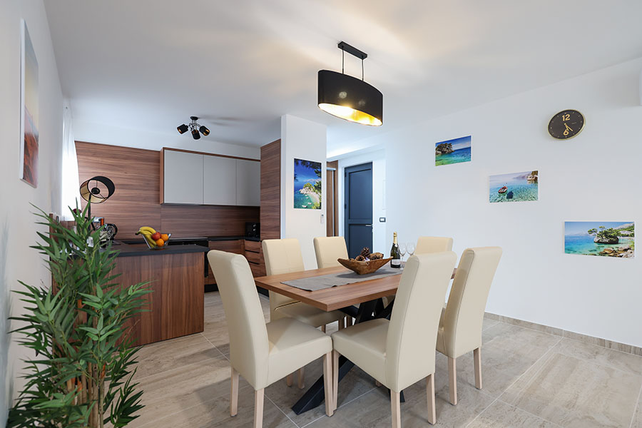 Moderna blagovaonica s drvenim stolom, krem stolicama i susjednom kuhinjom, karakteristična za luksuzni smještaj s minimalističkim dizajnom