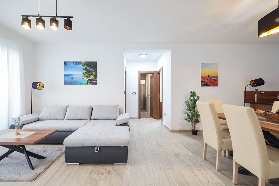 Moderan i svijetao dnevni boravak i blagovaonica s udobnom L-oblikovanom sofom, stolićem za kavu i elegantnim blagovaonskim setom, karakterističan za luksuzni smještaj