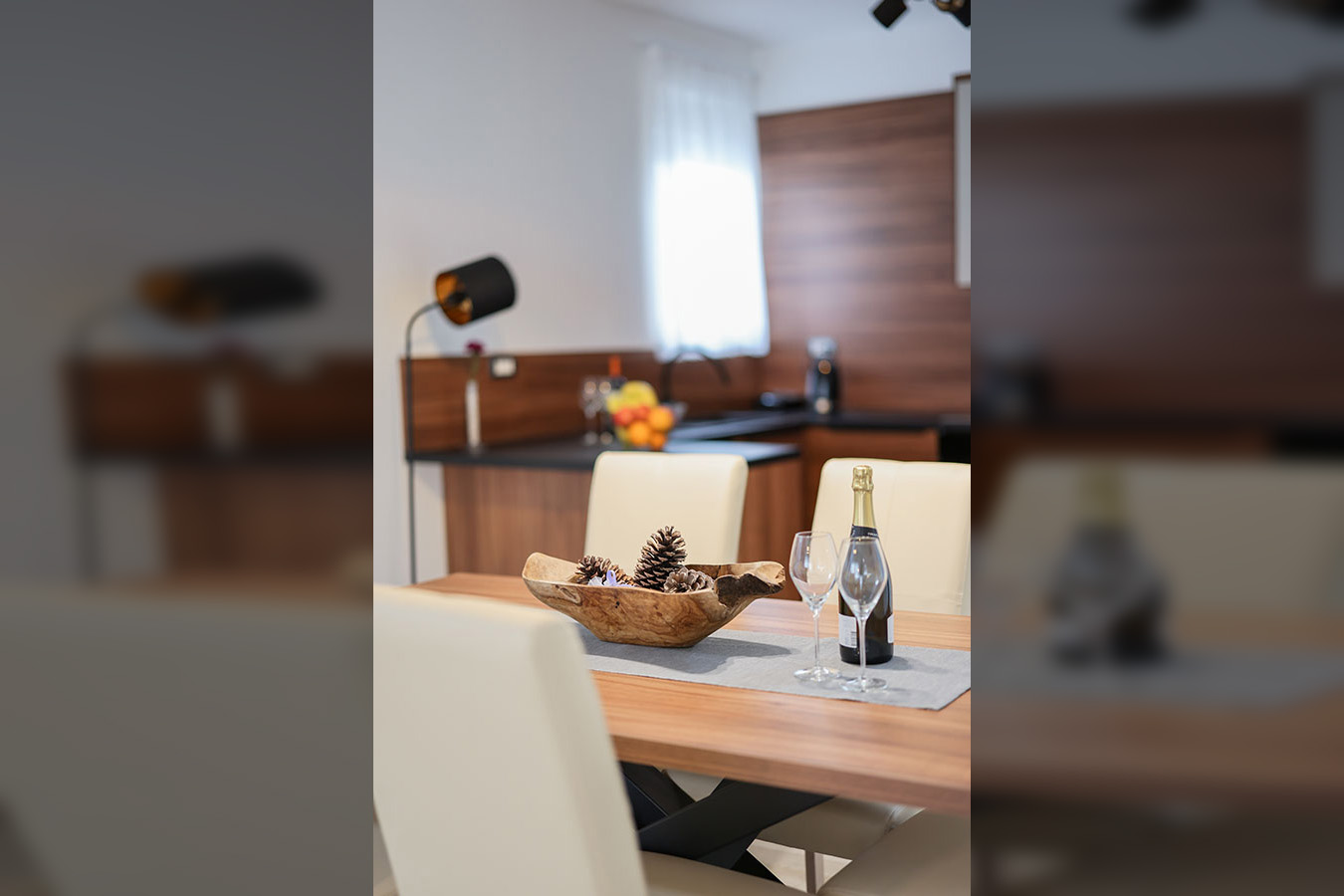 Moderna i elegantna blagovaonica, s drvenim stolom postavljenim bocom šampanjca, dvjema čašama i ukrasnom zdjelom borovih češera, odražavajući kvalitetu luksuznog smještaja