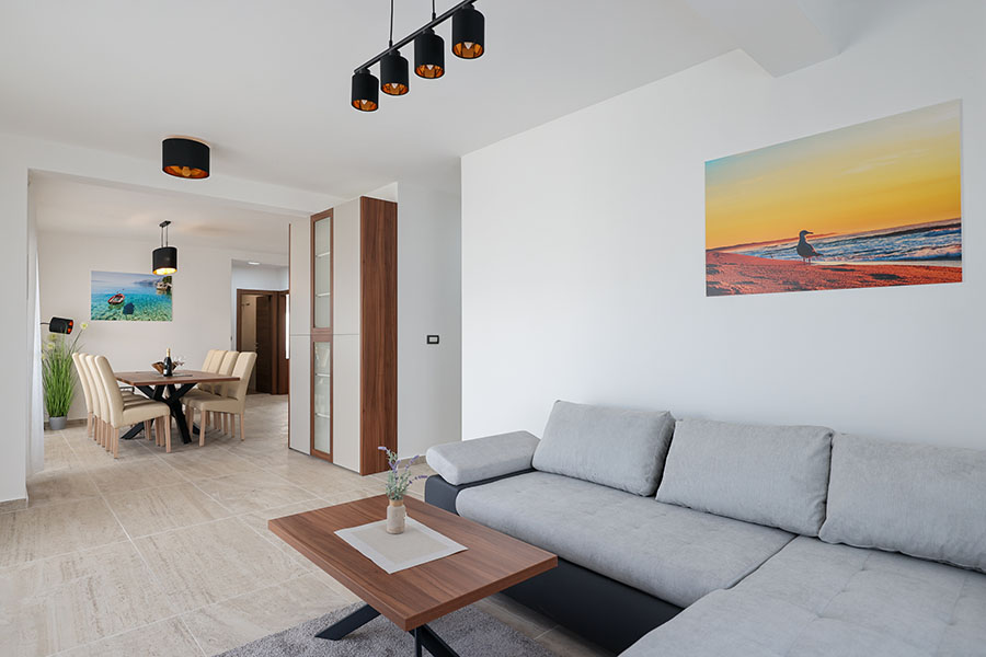 Prostran i svijetao dnevni boravak i blagovaonica, s udobnom sivom kutnom garniturom, drvenim stolićem za kavu i blagovaonskim setom s tapeciranim stolicama, primjer luksuznog smještaja