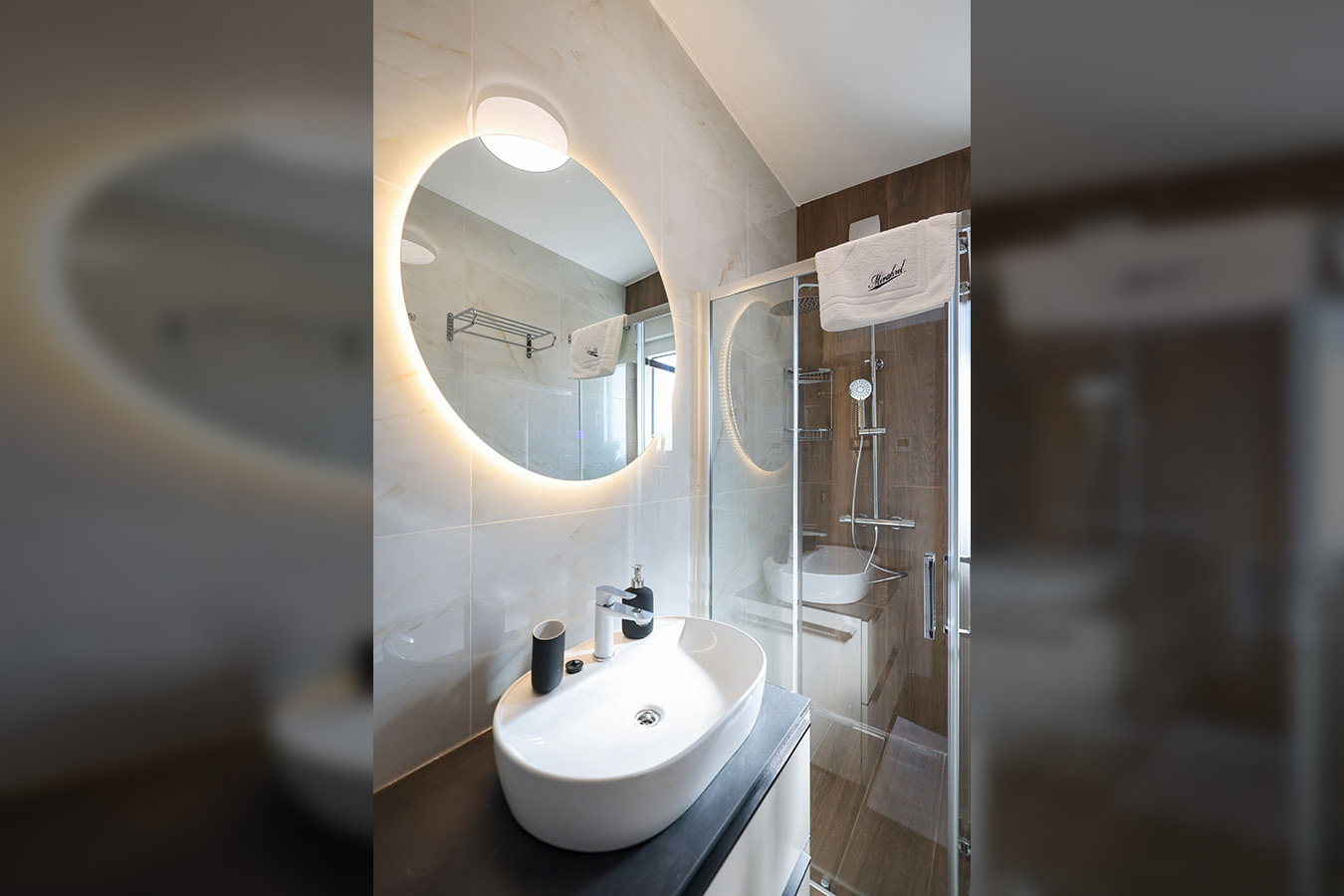 Elegantna kupaonica s osvijetljenim ogledalom, modernim umivaonikom i staklenom tuš kabinom, idealna za luksuzni smještaj