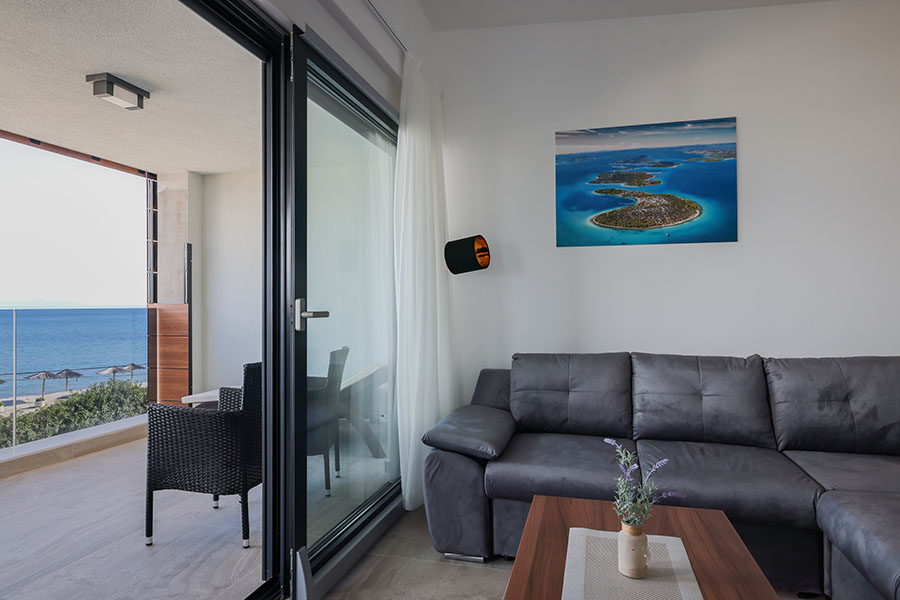Moderan dnevni boravak s udobnom sivom sofom i balkonom s pogledom na more i plažu, savršen za luksuzni smještaj