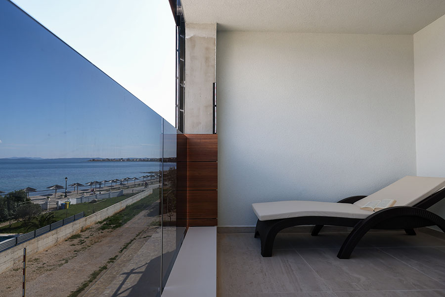 Moderan balkon s udobnom ležaljkom i prekrasnim pogledom na more, nudeći luksuzni smještaj idealan za opuštanje