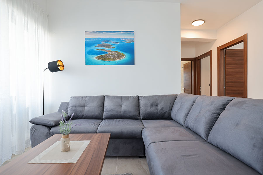 Moderan i svijetao dnevni boravak s udobnom sivom kutnom garniturom i impresivnom zračnom slikom otoka, savršen za luksuzni smještaj
