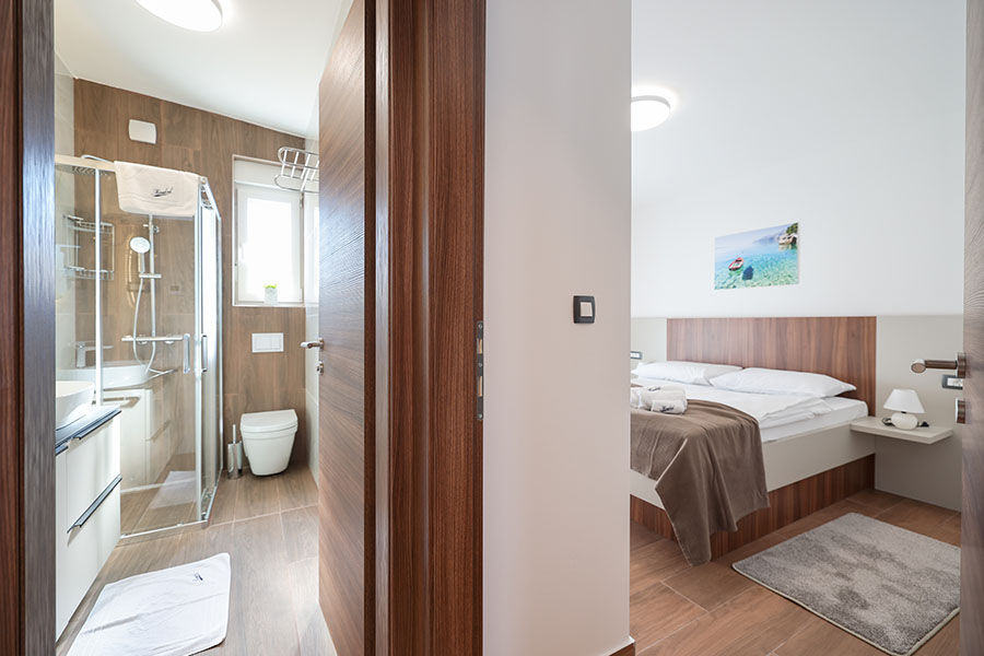 Udobna spavaća soba i moderna kupaonica, tipični detalji za apartmane Vir, prikazani kroz otvorena vrata