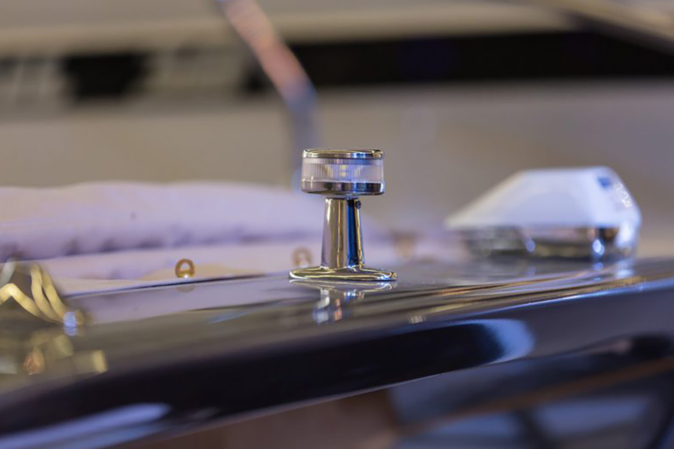 Detaljan prikaz navigacijskog svjetla s poliranom kromiranom bazom i prozirnim bijelim vrhom, odrazujući se na sjajnoj površini luksuznog gumenjaka