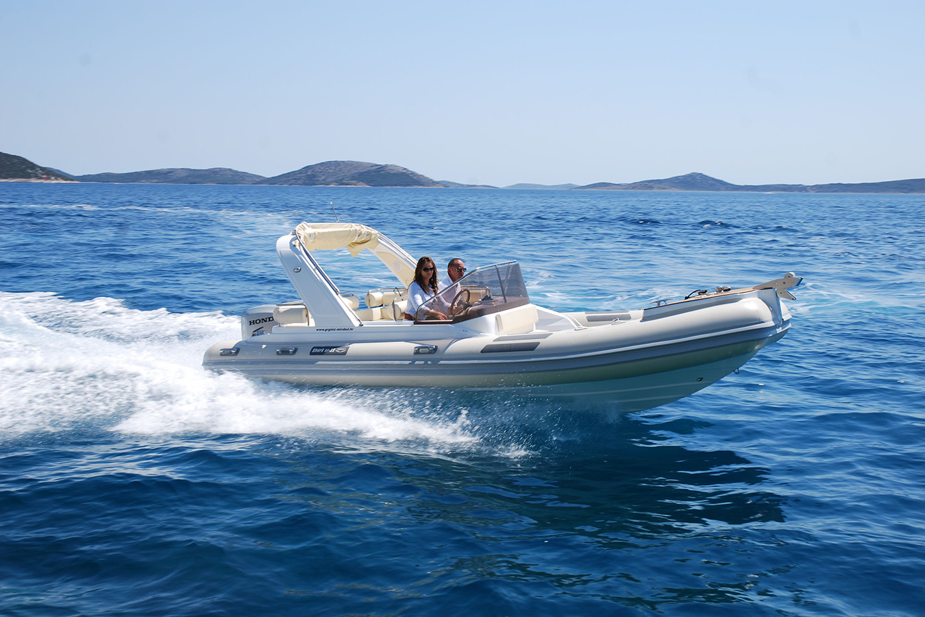 Par plovi luksuznim gumenjakom po plavom moru za sunčanog dana, s otocima u pozadini