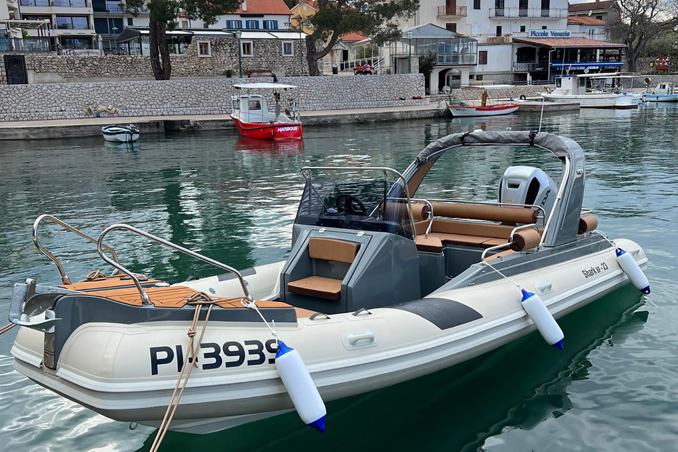 Moderan, bijelo-sivi luksuzni gumenjak usidren u mirnoj luci s obalnim zgradama u pozadini