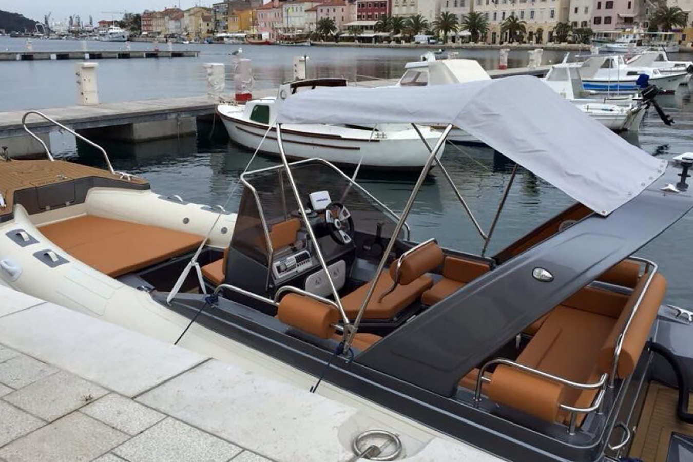 Elegantan luksuzni gumenjak s udobnim smeđim sjedalima i bijelom tendom, privezan u slikovitoj marini