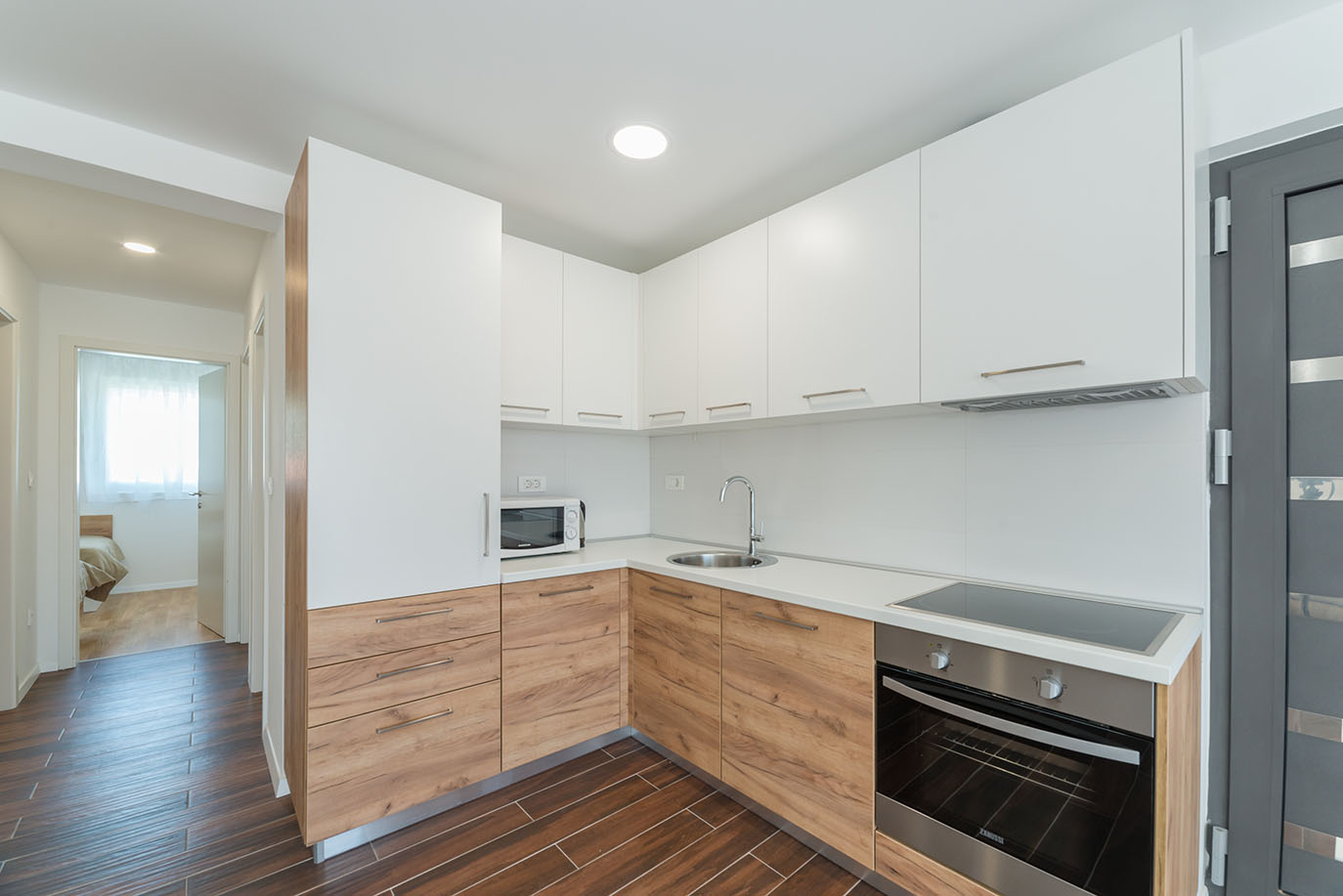 Čista i moderna kuhinja s bijelim gornjim ormarićima, drvenim donjim ormarićima, mikrovalnom pećnicom, pećnicom i sudoperom, često prisutna u kvalitetnim apartmanima Vir