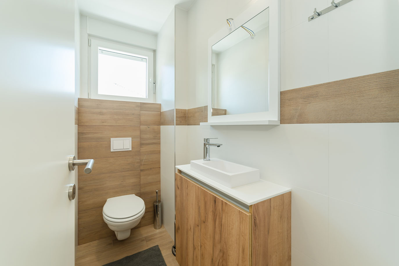 Svijetla i moderna kupaonica s pločicama izgleda drva i bijelim pločicama, sa suvremenim umivaonikom, WC-om i ogledalom, što je karakteristika luksuznih apartmana u Hrvatskoj