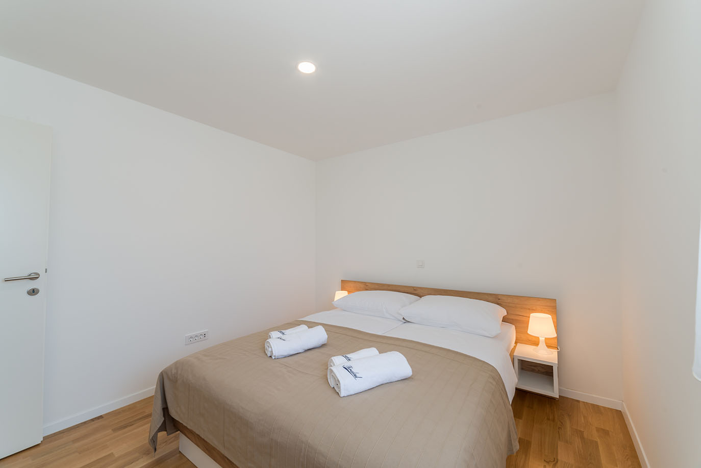 Svijetla i moderna spavaća soba s bračnim krevetom, bijelom posteljinom i noćnim lampama, tipična za kvalitetne apartmane u Viru