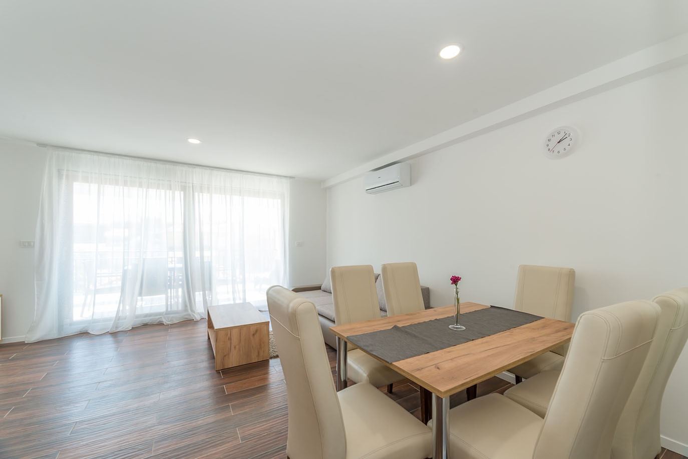 Svijetli i moderni blagovaonski i dnevni prostor u apartmanima Vir, s drvenim stolom, krem stolicama i pristupom balkonu sa prozirnim zavjesama