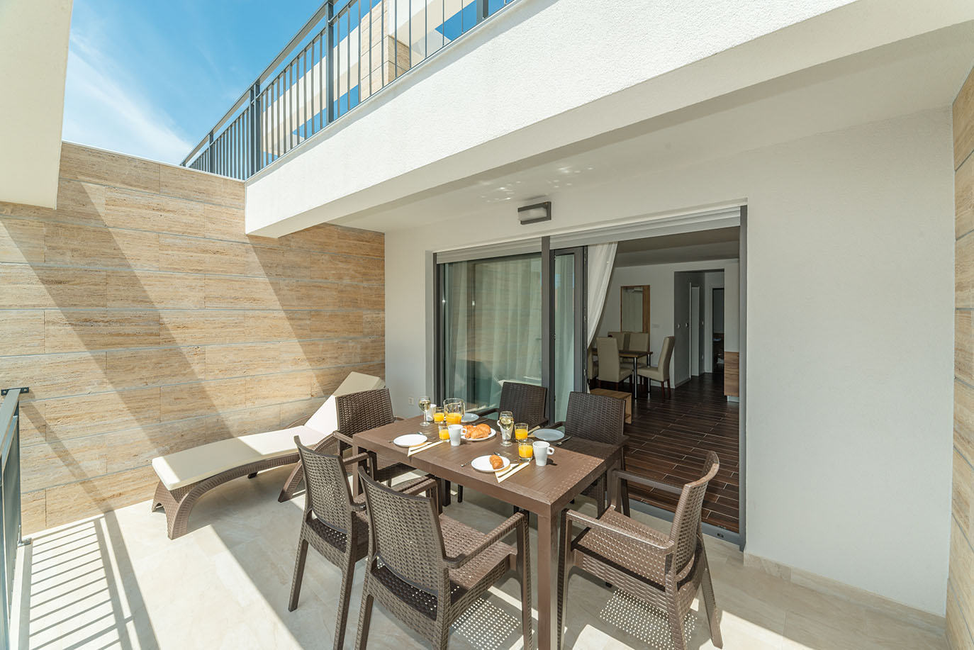 Sunčana vanjska terasa apartmana Vir s blagovaonskim stolom postavljenim za doručak, pletenim stolicama i udobnom ležaljkom