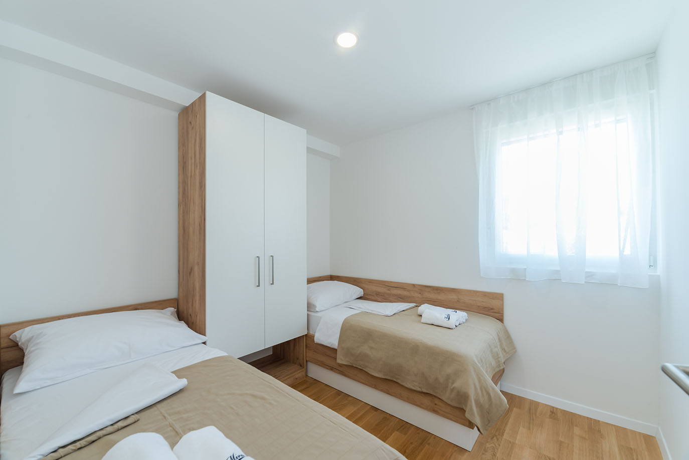 Svijetla spavaća soba s dva odvojena kreveta, ormarom i prozorom, tipična za udobne apartmane na Viru