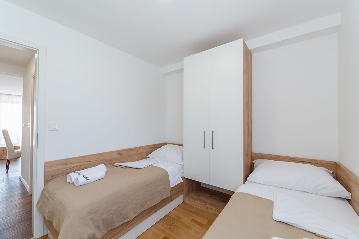 Svijetla, moderna dvokrevetna spavaća soba s dva pojedinačna kreveta s drvenim okvirima i bijelim ormarom, tipična za udoban smještaj u Villi Mirakul
