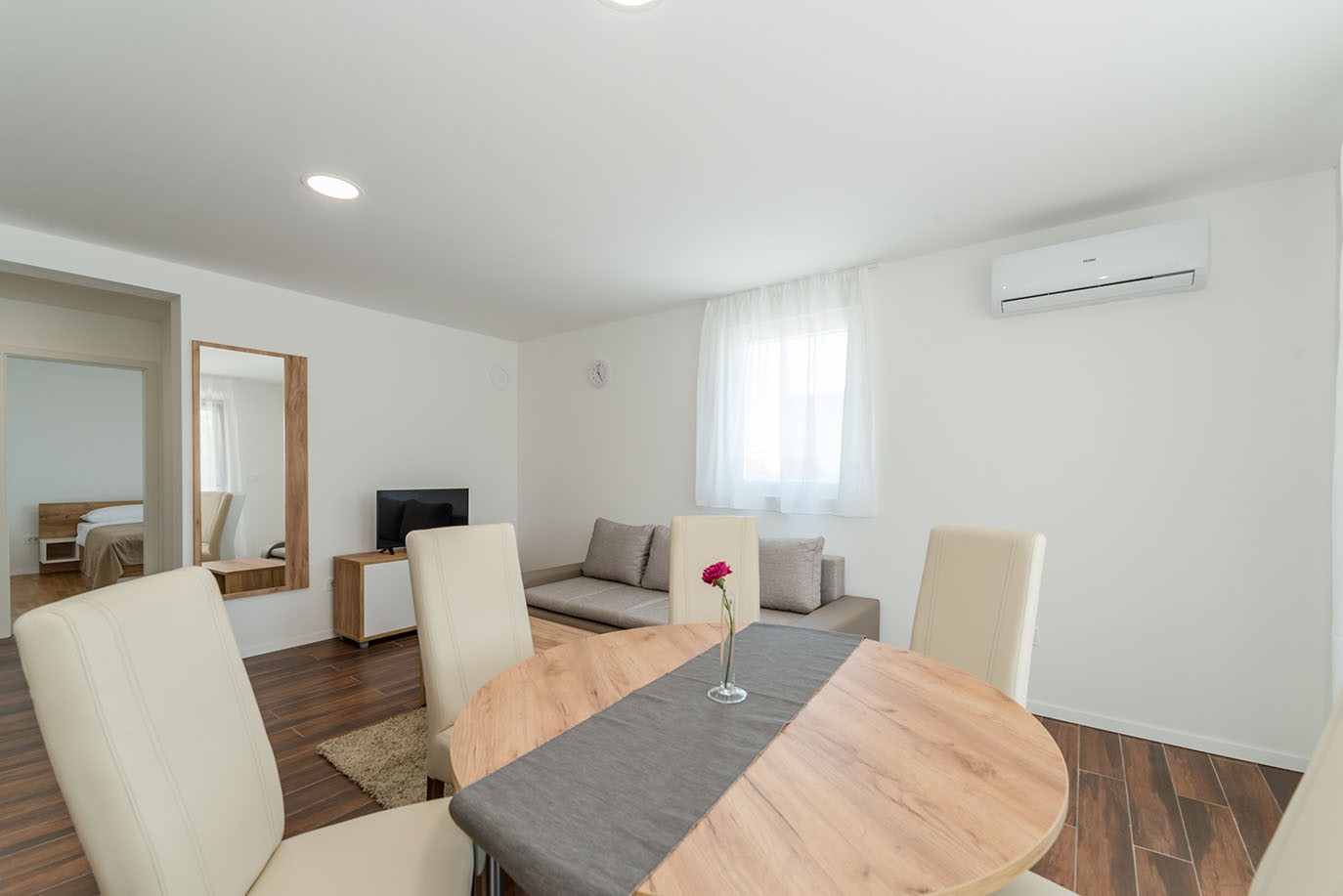 Moderna blagovaonica i dnevni boravak s okruglim drvenim stolom, udobnim sjedećim garniturama i klima uređajem, prikazujući unutrašnjost privlačnog apartmana na Viru