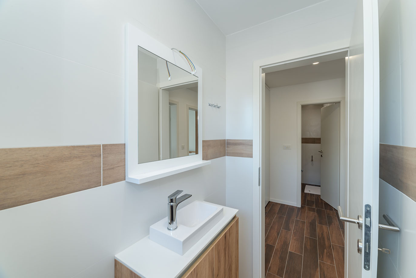 Moderna kupaonica s bijelim pravokutnim umivaonikom, kromiranom slavinom i velikim ogledalom iznad drvenog ormarića, u stilu kakav nude apartmani Vir