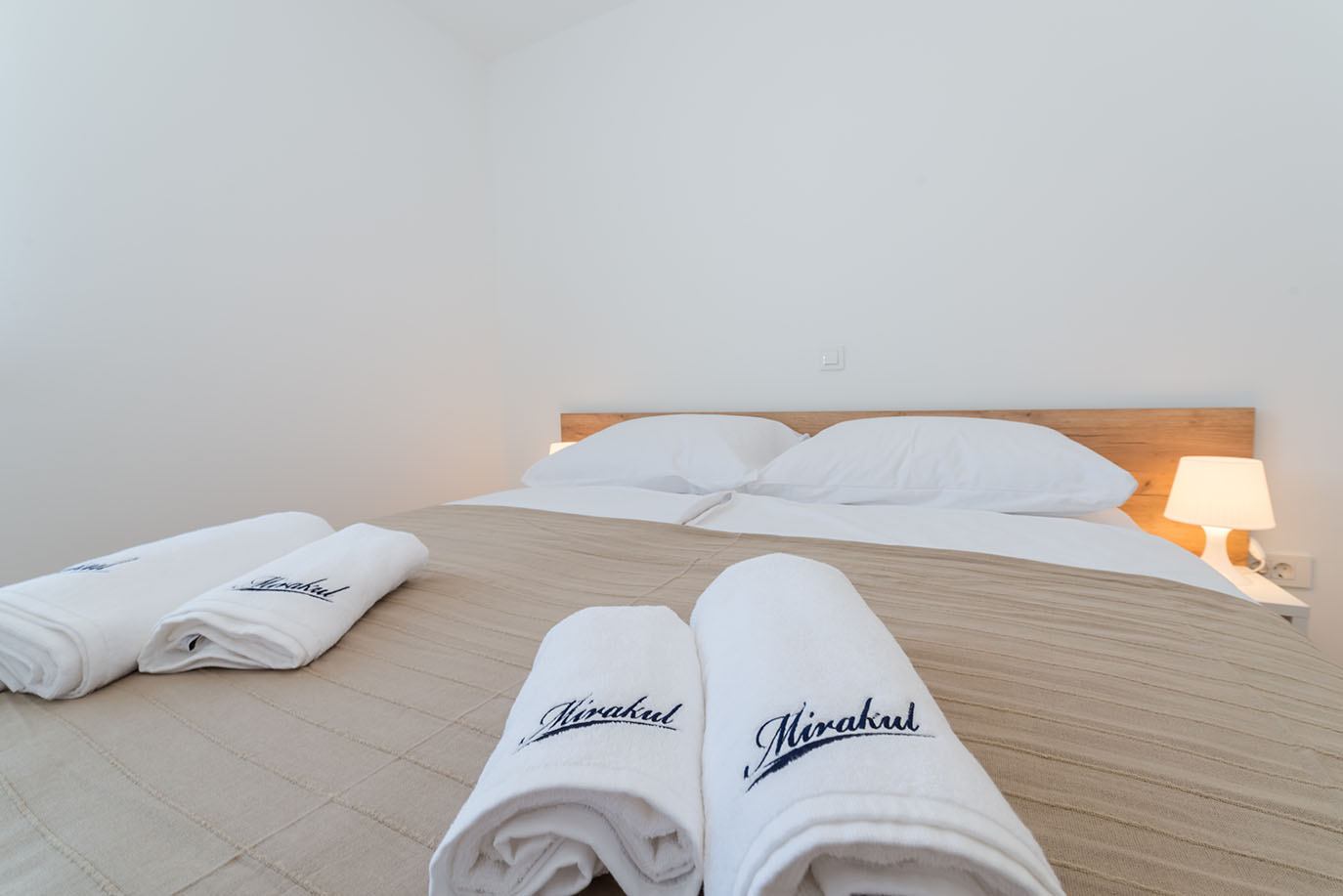 Udoban bračni krevet s bijelom posteljinom i uredno složenim ručnicima s natpisom 'Mirakul' u svijetloj spavaćoj sobi vile Mirakul
