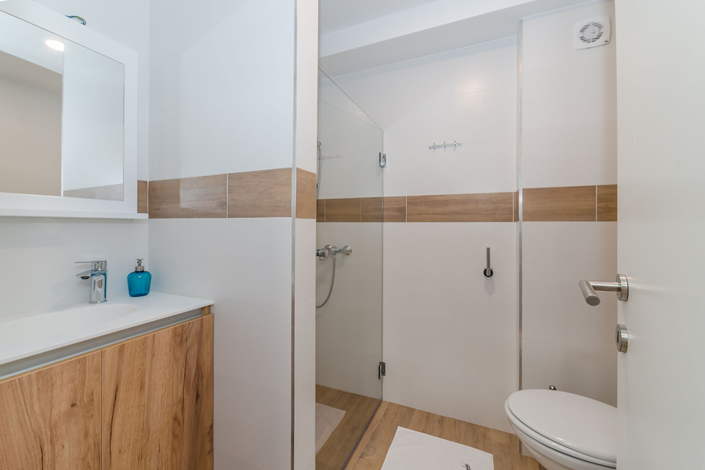 Moderna i čista kupaonica s drvenim ormarićem, bijelim umivaonikom, ogledalom, staklenom tuš kabinom i WC-om, prikazujući kvalitetu smještaja u apartmani Vir