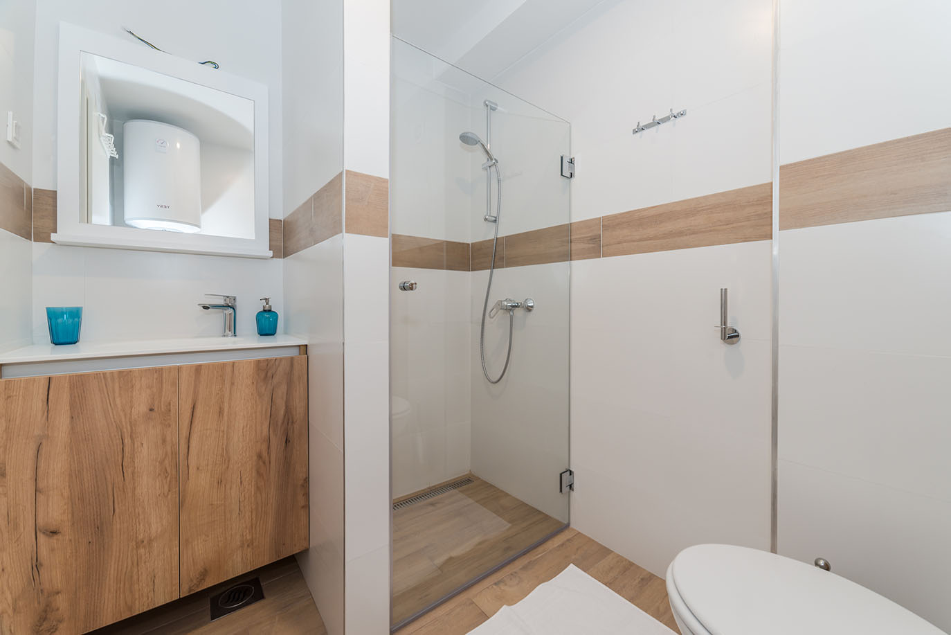 Svijetla i moderna kupaonica s tuš kabinom, drvenim ormarićem s umivaonikom i WC-om, tipična za apartmane Vir