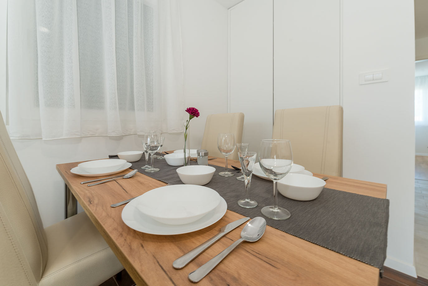 Svijetla blagovaonica s drvenim stolom postavljenim bijelim posuđem, čašama i priborom za jelo, prikazujući udoban prostor u tipičnom apartmanu Vir