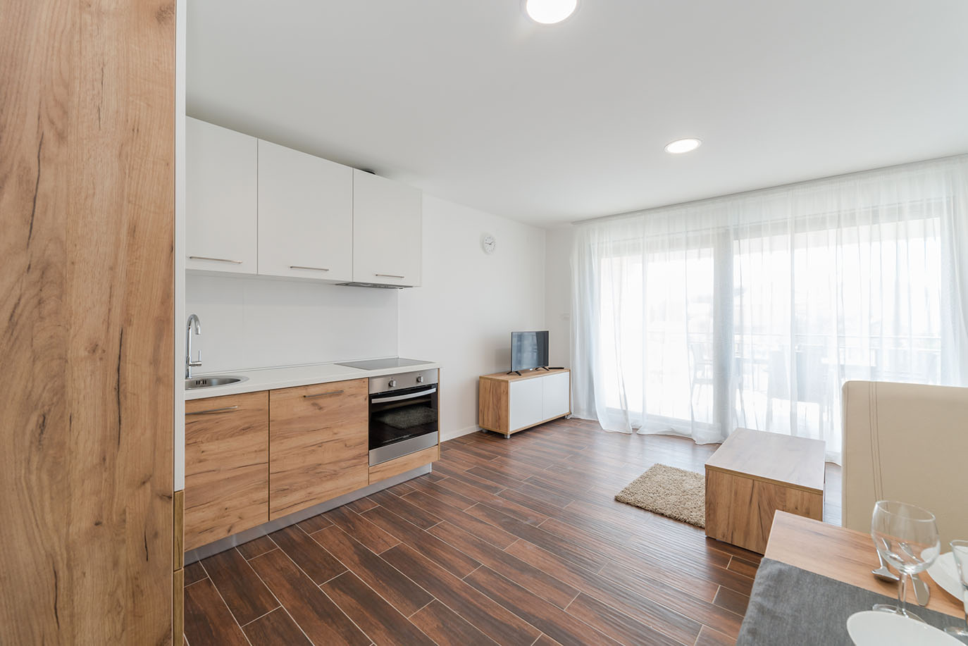 Prostrana i moderna kuhinja otvorenog plana s dnevnim boravkom u apartmanu Villa Mirakul, s ormarićima boje svijetlog drva i obiljem prirodnog svjetla