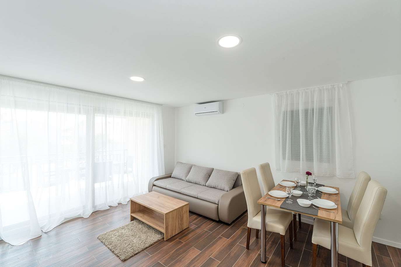 Svijetao i moderan otvoreni prostor dnevnog boravka i blagovaonice s udobnom sofom, drvenim stolićem za kavu i blagovaonskim stolom postavljenim za četiri osobe, što je tipično za ugodne apartmane Vir