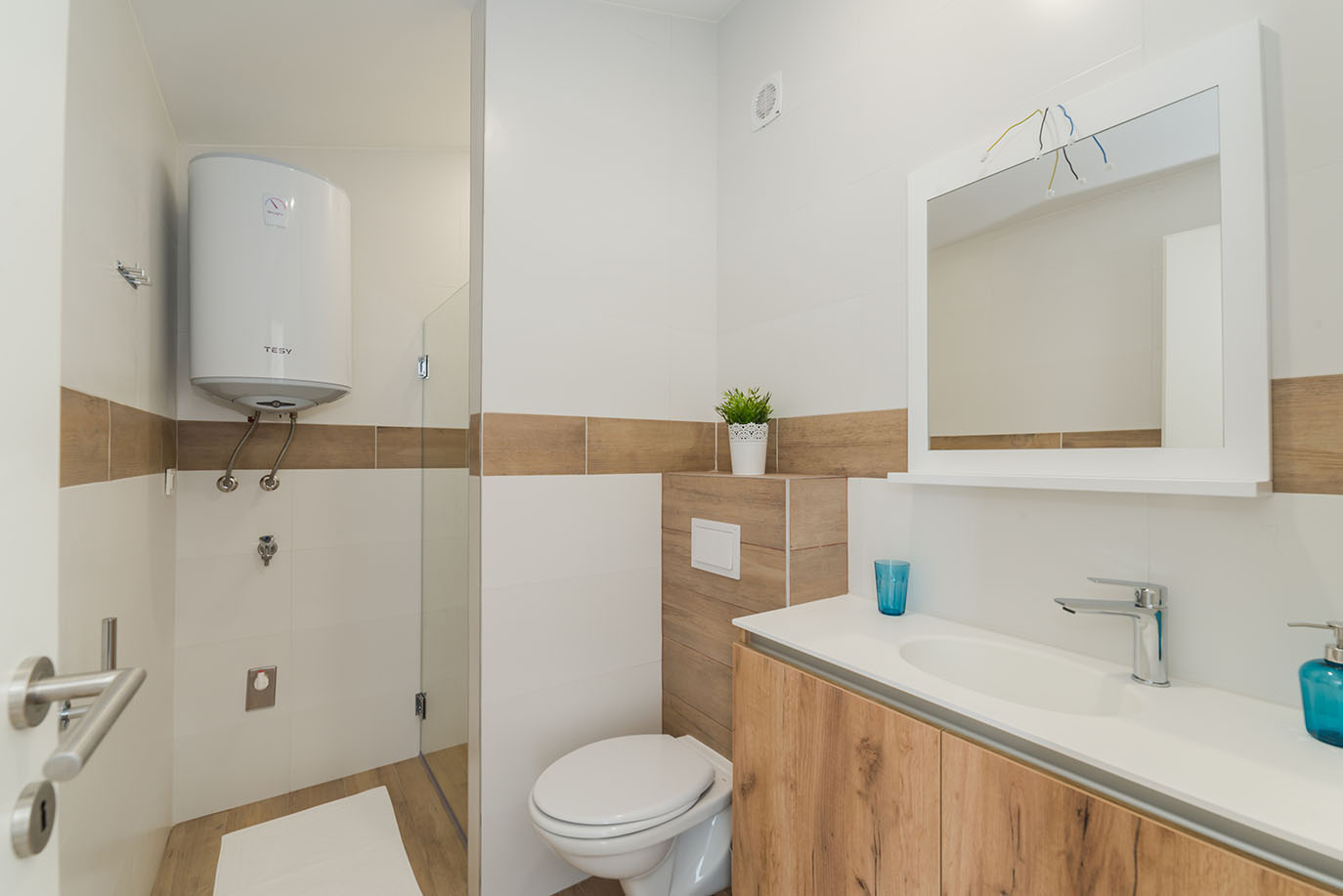 Moderna kupaonica s tušem, WC-om i umivaonikom, obložena bijelim i drvenim pločicama, tipična za apartmani Vir