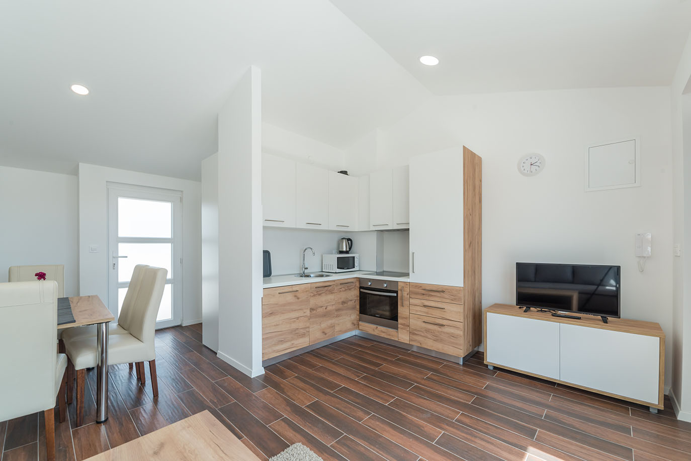 Svijetao, moderan otvoreni prostor kuhinje i dnevnog boravka s blagovaonskim stolom i TV-om, tipičan za kvalitetne apartmane Vir