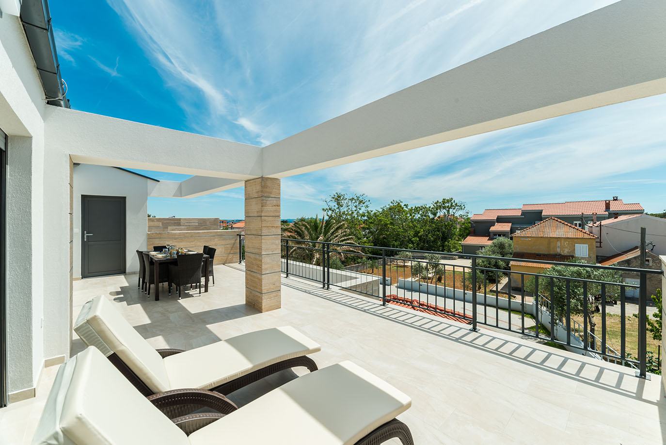 Prostrana krovna terasa Ville Mirakul s ležaljkama, vanjskom blagovaonicom i slikovitim pogledom na grad, drveće i more pod vedrim plavim nebom