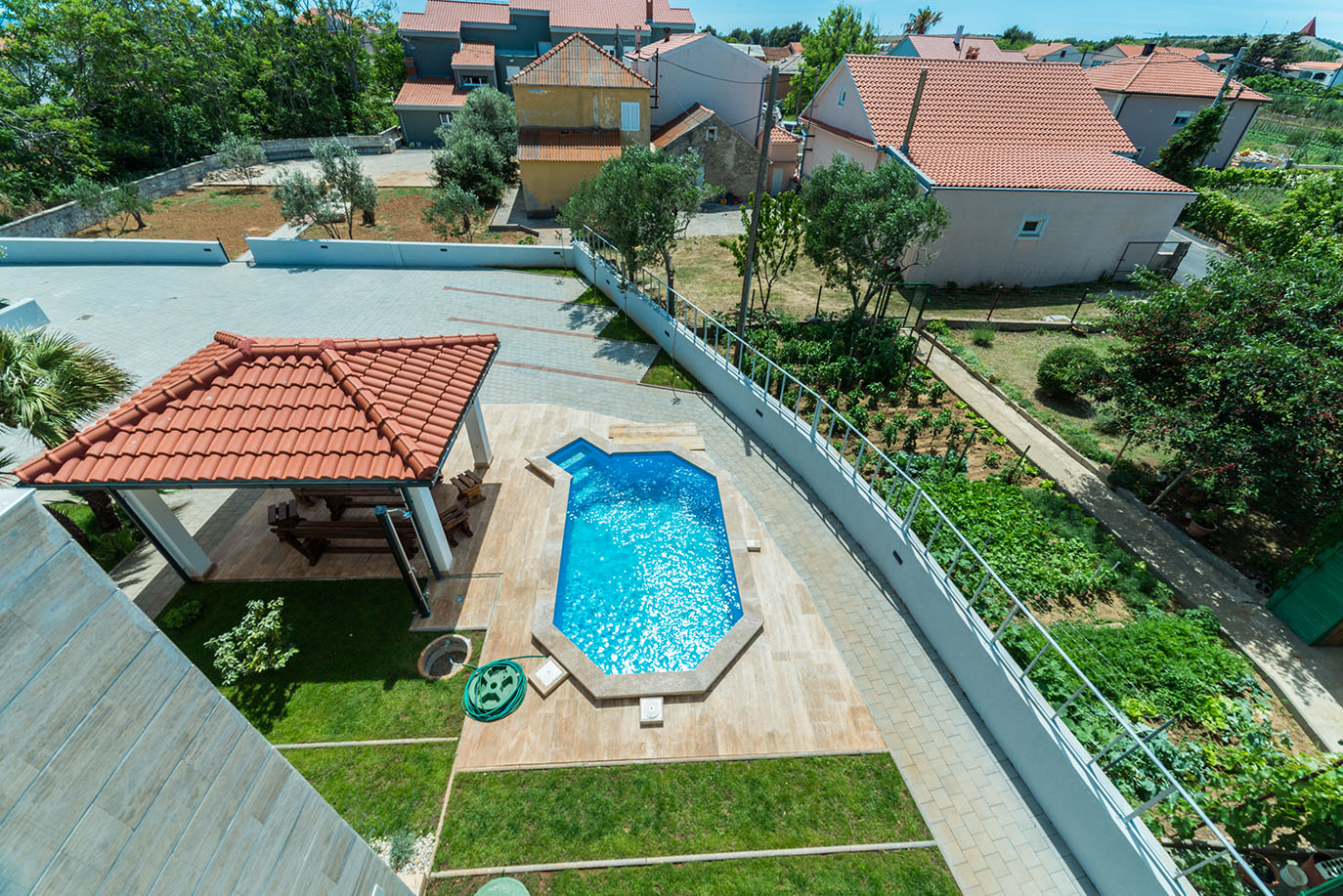 Prikaz iz zraka smještaja za odmor koji uključuje svjetlucavi plavi bazen, sjenicu s crvenim krovom za blagovanje na otvorenom, zelene travnjake i uredan povrtnjak, savršeno za apartmani Vir