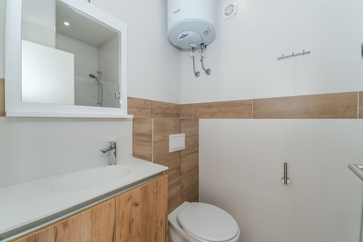 Uredna i moderna kupaonica s bijelim umivaonikom, drvenim ormarićem, ogledalom, WC-om i bojlerom, tipična za kvalitetne apartmane Vir