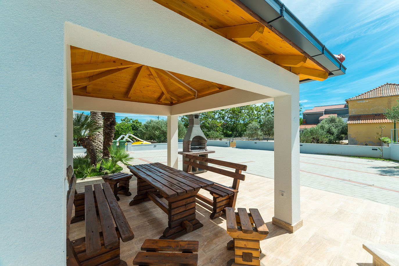 Privlačno vanjsko dvorište s robusnim drvenim stolom za objedovanje i klupama te zidanim roštiljem, idealno mjesto za opuštanje u Villa Mirakul